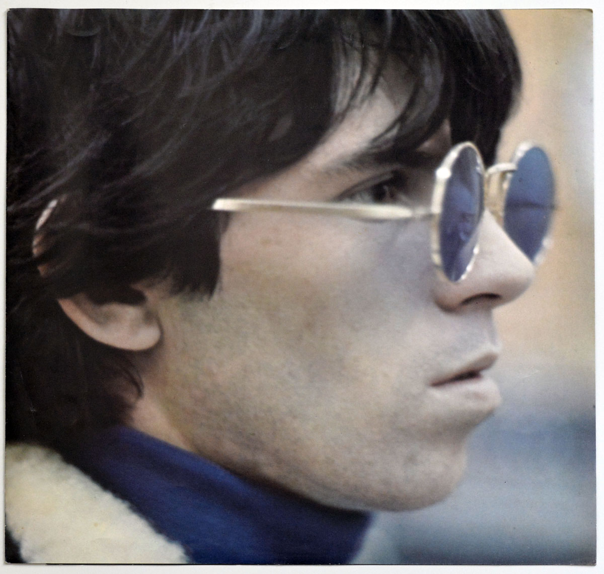 Profile close-up of Keith Richards in the 1974 German edition of Rolling Stones’ Big Hits, wearing reflective blue-tinted round sunglasses, with tousled black hair and dressed in a deep blue turtleneck under a cream shearling coat.